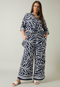 Blusa de rayas en azul marino y crema con botones en el frente y bolsillos, combinada con pantalones de pierna ancha a juego que cuentan con una cinturilla elástica.