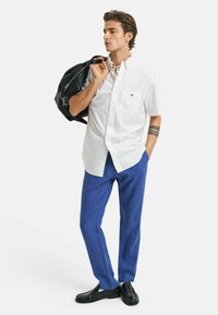 Witte short-sleeve shirt met zak, blauwe broek, zwarte tas en zwarte schoenen. Kenmerkt een gestreepte halsdoek en een polstatoeage.