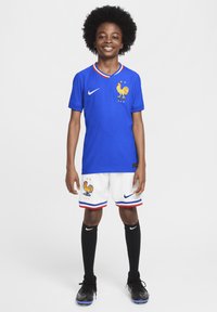 Camisa de fútbol azul con cuello a rayas y emblema de gallo, acompañada de pantalones cortos blancos con acentos en azul y rojo, calcetines negros y zapatos.