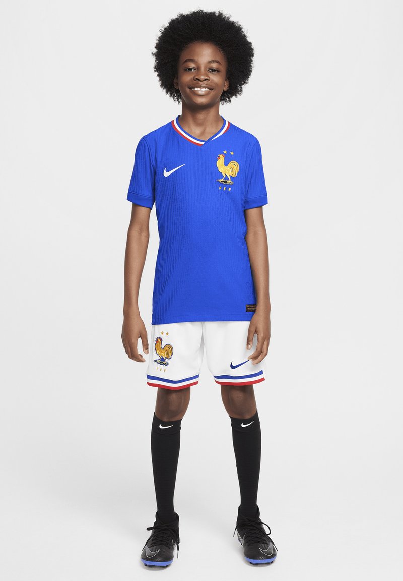 Camisa de fútbol azul con cuello a rayas y emblema de gallo, acompañada de pantalones cortos blancos con acentos en azul y rojo, calcetines negros y zapatos.