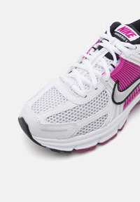 La chaussure de course Nike Vomero 5 présente une tige en mesh blanche avec des accents roses, un logo noir et une semelle texturée pour une meilleure adhérence. Les lacets sont blancs.