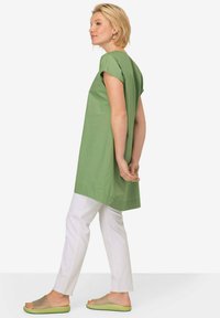 Zelená tunika s krátkými rukávy, lehká tkanina, boční rozparky, kombinovaná s bílými zúženými kalhotami a průsvitnými zelenými sandály.