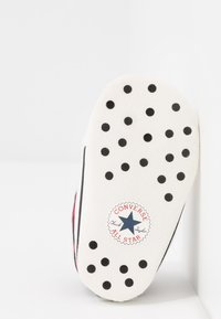 Biała gumowa podeszwa w czarne kropki, z czerwoną i niebieską logo Converse All Star na środku. Czysty, prosty design.