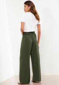 Olivgröna vida byxor med elastisk midja, kombinerade med en vit kortärmad t-shirt. Slät tyg med skräddarsydd passform.