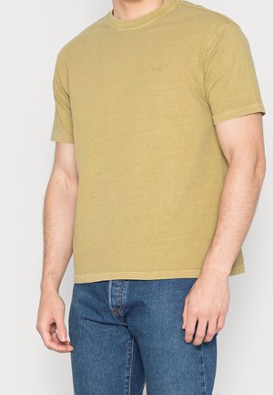 T-shirt z krótkim rękawem i okrągłym dekoltem w kolorze oliwkowej zieleni, wykonany z bawełny. Na piersi subtelne haftowane logo. W zestawie z niebieskimi dżinsami.