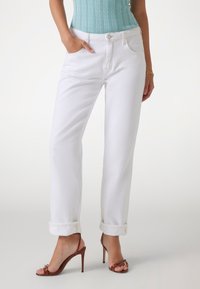 Jeans bianchi a gamba dritta con orli arrotolati, design a cinque tasche e dettagli di cucitura sottili. Abbinati a sandali alti con cinturini marroni.