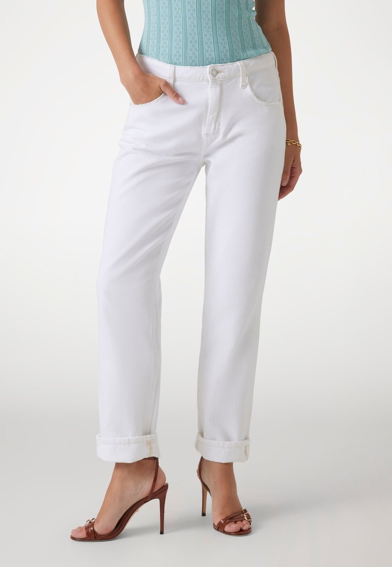 Jeans bianchi a gamba dritta con orli arrotolati, design a cinque tasche e dettagli di cucitura sottili. Abbinati a sandali alti con cinturini marroni.