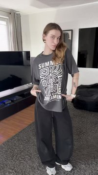 Grijze T-shirt met witte opdruk met de tekst "SUMMER DREAMING" en abstracte ontwerpen. Losse pasvorm gecombineerd met zwarte brede broekspijpen en sneakers.