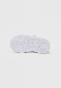 Λευκή σόλα αθλητικού παπουτσιού με υφή από καουτσούκ και ζιγκ ζαγκ σχέδια, καθώς και στρογγυλεμένη φτέρνα. Το λογότυπο της μάρκας είναι ορατό στο πλάι.