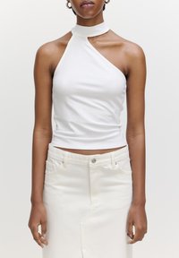 Witte geribbelde haltertop met een hoge hals, met een asymmetrisch ontwerp. Draagt een hoogstaande witte denimrok.