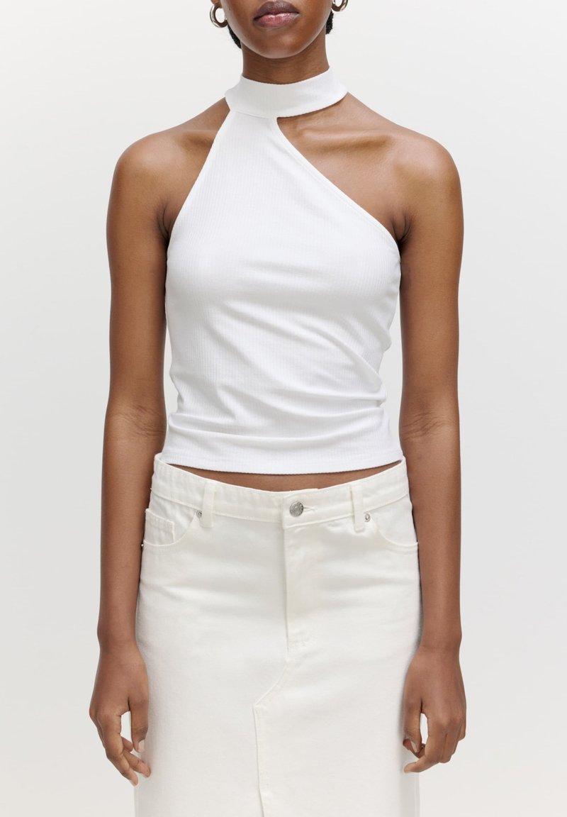 Witte geribbelde haltertop met een hoge hals, met een asymmetrisch ontwerp. Draagt een hoogstaande witte denimrok.