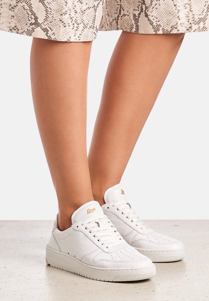 Bílé kožené tenisky s perforovanými detaily, kulatou špičkou, šněrováním a texturovanou gumovou podrážkou. Zlaté logo na jazyku.
