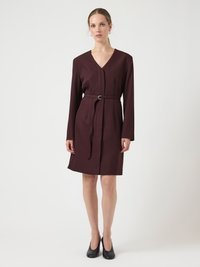 Φόρεμα μπορντό τύπου wrap με μακριά μανίκια, V-λαιμόκοψη και ζώνη στη μέση. Λεία υφή, μήκος μέχρι το γόνατο, φορεμένο με μαύρες γόβες.
