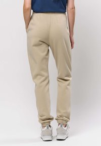 Beiga träningsbyxor med elastisk midja och muddar, gjorda av mjukt tyg. Har sidfickor och en avslappnad passform. Bärs med grå sneakers.