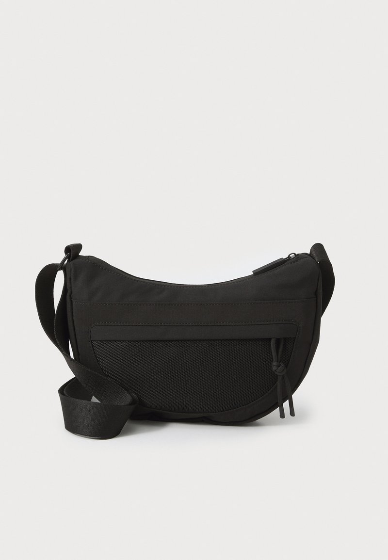 Schwarze Stofftasche mit geschwungener Form, verstellbarem Tragegurt, strukturiertem Vorderteil und Reißverschlussverschluss. Mit einem dekorativen Knoten-Detail.