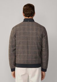 Chaqueta bomber de cuadros marrones con un cuello y puños de punto en color azul marino. Presenta una tela texturada y un diseño ajustado. La vista trasera muestra un patrón distintivo.