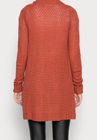 Cardigan a maglia color ruggine con un motivo testurizzato, maniche lunghe e polsini a costine. Il design presenta un retro più lungo e lati aderenti.