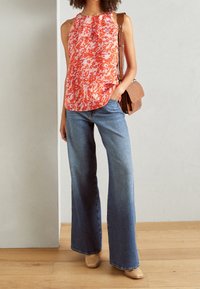 Top senza maniche con motivo floreale arancione e bianco, abbinato a jeans svasati azzurri chiari. Completo con una borsa a spalla marrone texturizzata.
