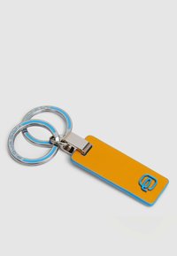 Sleutelhanger met een rechthoekig geel lichaam met een blauwe omlijsting, zilveren beslag en twee gekoppelde ringen. Logo in blauw geëtst.