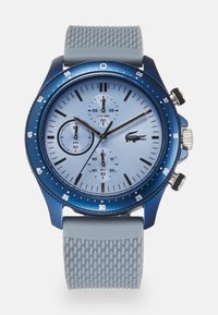 Reloj cronógrafo analógico azul con una esfera azul claro, correa de goma texturizada gris y tres subesferas para minutos, segundos y décimas de segundo.