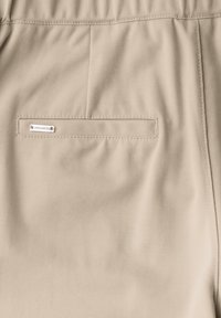 Beige shorts dengan bahan bertekstur, dilengkapi dengan kantong belakang dan tag logo logam kecil. Pinggangnya elastis untuk kenyamanan.
