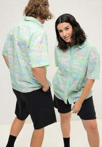 Kortærmet skjorte i lysegrøn med et farverigt blomsterdesign, parret med sorte shorts. Har en knap-åbning og en afslappet pasform.