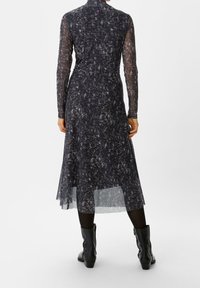 Schwarzes Kleid mit langen durchsichtigen Ärmeln, einem abstrakten weißen und rosa Muster, einem hohen Ausschnitt und einem fließenden Saum, kombiniert mit schwarzen knöchelhohen Stiefeln.