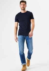 Camiseta ajustada azul marino, jeans rectos azul claro y botas de trabajo marrón claro. Un look casual con los puños arremangados y un detalle mínimo.
