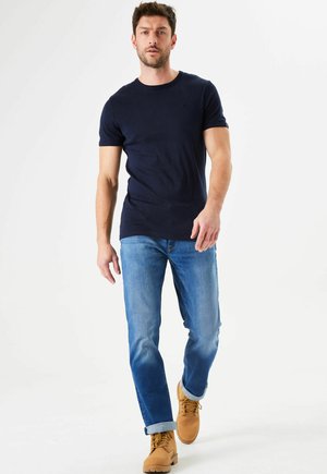 Camiseta ajustada azul marino, jeans rectos azul claro y botas de trabajo marrón claro. Un look casual con los puños arremangados y un detalle mínimo.