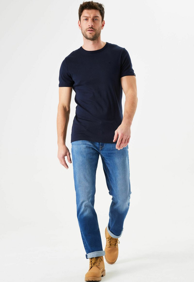 Camiseta ajustada azul marino, jeans rectos azul claro y botas de trabajo marrón claro. Un look casual con los puños arremangados y un detalle mínimo.