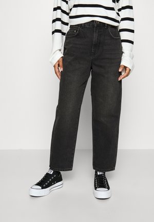 Osoba nosząca czarne dżinsy z wysokim stanem o prostych nogawkach, czarno-białe trampki oraz białą koszulę z długim rękawem i czarnymi poziomymi paskami.