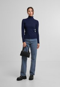 Granatowy sweter z wysokim kołnierzem w prążki, jasnoniebieskie proste dżinsy, czarne buty na grubej podeszwie oraz mała czarna torebka z metalowymi akcentami w kolorze srebra.