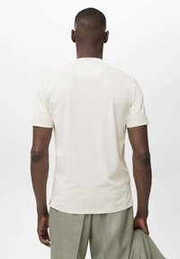T-shirt a maniche corte, di colore crema uniforme, con colletto a girocollo e una texture liscia. Viene mostrato il retro, con cuciture o dettagli minimi visibili.