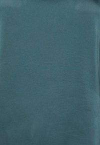 Teal tyg med en slät textur som har en subtil lyster. Designen är minimalistisk, utan synliga mönster eller hårdvara.