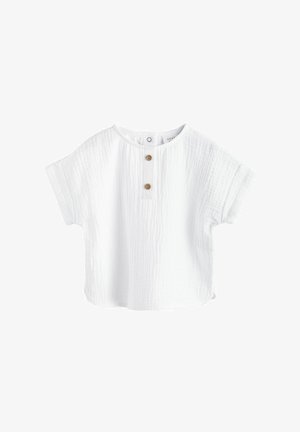 Valge lühikeste varrukatega pluus, mis on valmistatud tekstuursetest puuvillast, ümara kaelusega ja millel on kaks puidust nuppu ees.