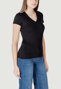 Maglietta nera aderente con scollo a V, maniche corte e una texture morbida. Abbinata a jeans blu, che mostrano un design informale.