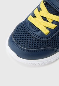 Blå sneaker i mesh og skinn med gule lisser og hvit såle. Overdelen har en pustende design og forsterkede sømmer.