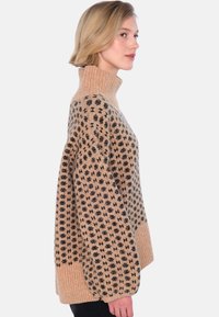 Beige stickad tröja med svart blommönster, hög krage och oversized passform; har ribbad textur på krage och fåll.