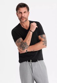 T-shirt noir à col en V associé à un pantalon à motifs gris clair. Comprend des tatouages corporels et une ceinture noire avec une boucle en argent.