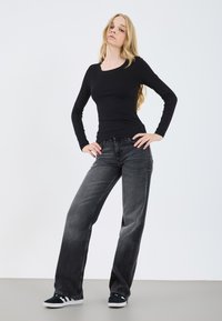 Zwarte geribbelde lange mouw top gecombineerd met losse donkergrijze jeans, met een lichte gradient en versleten textuur; gedragen met zwart-witte sneakers.