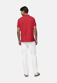Camisa polo roja con mangas cortas, de material de algodón, combinada con pantalones blancos. Incluye un cuello clásico y un corte relajado.