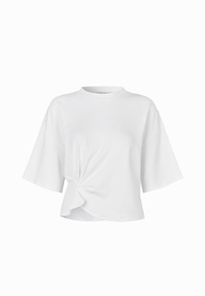 Fehér rövidujjú póló sima pamutból. Kerek nyakkal és elöl egy csomózott részlettel rendelkezik, ami aszimmetrikus formát ad neki.