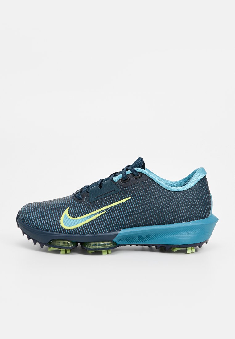 Donkerblauwe Nike trainingsschoen met een geperforeerde mesh bovenwerk, neongele swoosh, lichtblauwe accenten en een dikke zool met groene details.