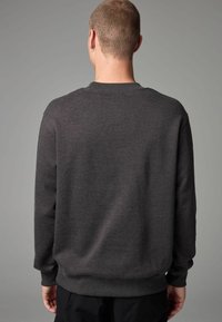 Dark gray sweatshirt, crew neck, ribbed cuffs and hem, soft texture, plain design, no visible patterns, worn with black pants.