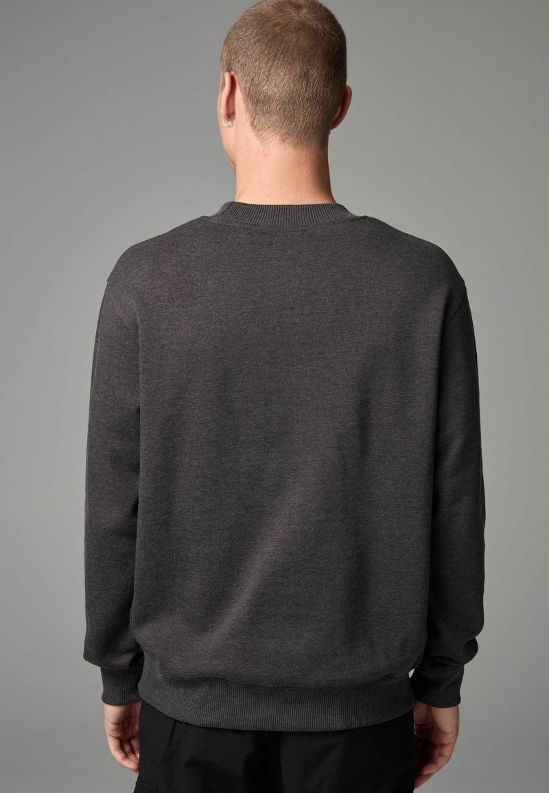Dark gray sweatshirt, crew neck, ribbed cuffs and hem, soft texture, plain design, no visible patterns, worn with black pants.