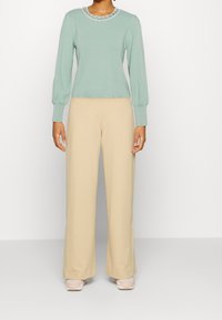 Maglione verde chiaro a maniche lunghe con dettaglio decorativo sul colletto abbinato a pantaloni beige a gamba larga. Tessuto morbido, vestibilità casual.