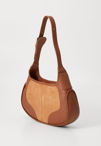 Brun læderhandtaske med en suing frontpanel, rund form, justerbar strop og glat tekstur med synlige syninger.