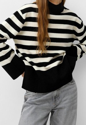 Pull en maille à rayures noir et blanc avec un col montant, des poignets et un ourlet côtelés. Associé à un pantalon en denim gris. Texture douce et coupe décontractée.