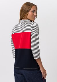 Gestreiftes Langarmoberteil mit einem roten Block und einem marineblauen unteren Abschnitt; aus weichem Stoff gefertigt, mit lockerer Passform und Rundhalsausschnitt.