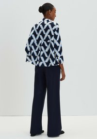 Giacca in stile kimono stampata in navy, bianco e azzurro chiaro con motivo geometrico; abbinata a pantaloni navy dal taglio ampio.